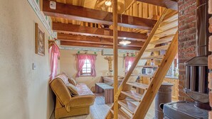 A rustic interior with a wooden staircase, a sofa, a table, and a wood-burning stove. - Vineyard Cottage Vesna Lake View (Cirkulane)