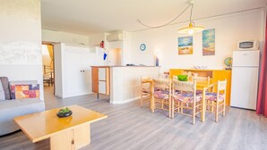 Un espacio habitable compacto con kitchenette, una zona de comedor con cuatro sillas, un sofá pequeño y una mesa de madera.