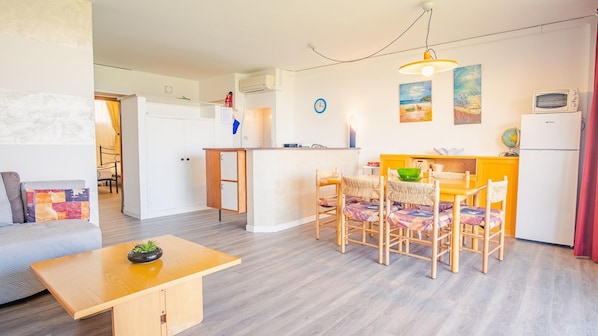 A compact living space with a kitchenette, a dining area with four chairs, a small sofa, and a wooden table.