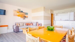 Una sala de estar moderna con un sofá, una mesa de comedor con sillas y una zona de cocina con armarios.