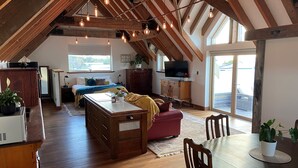 A spacious loft with a high ceiling, exposed wooden beams, a dining area with a round table and chairs, a cozy seating area with a red sofa, and a television mounted on the wall. - The Loft at Tulka House. The Seafood capital of South Australia. (Tulka)