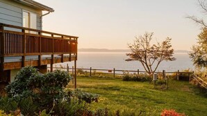 Ein Küstenanwesen mit einer Holzterrasse mit Blick auf das Meer, üppigem Grün und freiem Blick auf den Horizont.