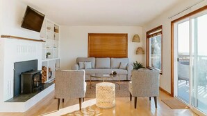 Ein modernes Wohnzimmer mit einer Couch, zwei Sesseln, einem Couchtisch, einem Kamin und einem großen Fenster.