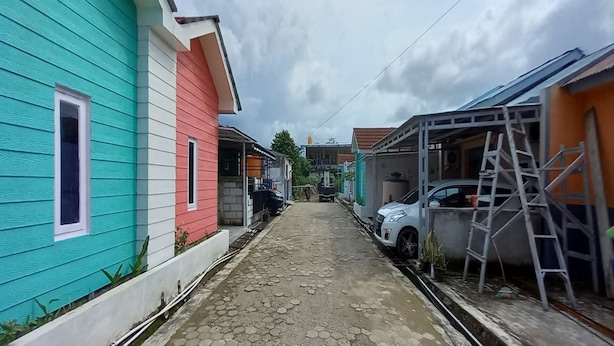 A narrow street with colorful houses, a white car, and construction materials. - OYO 90974 Homestay Golo Koe Sejahtera (Labuan Bajo)