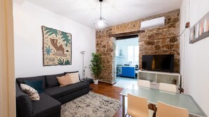 A modern living room with a black sectional sofa, a glass dining table with chairs, a stone accent wall, and a kitchen visible through an open doorway. - La Pietra al Pigneto (Rome)