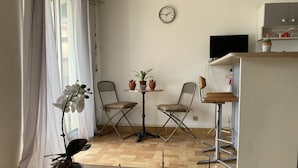 A compact living space with a dining area, two chairs, a small table, a clock, and a TV.