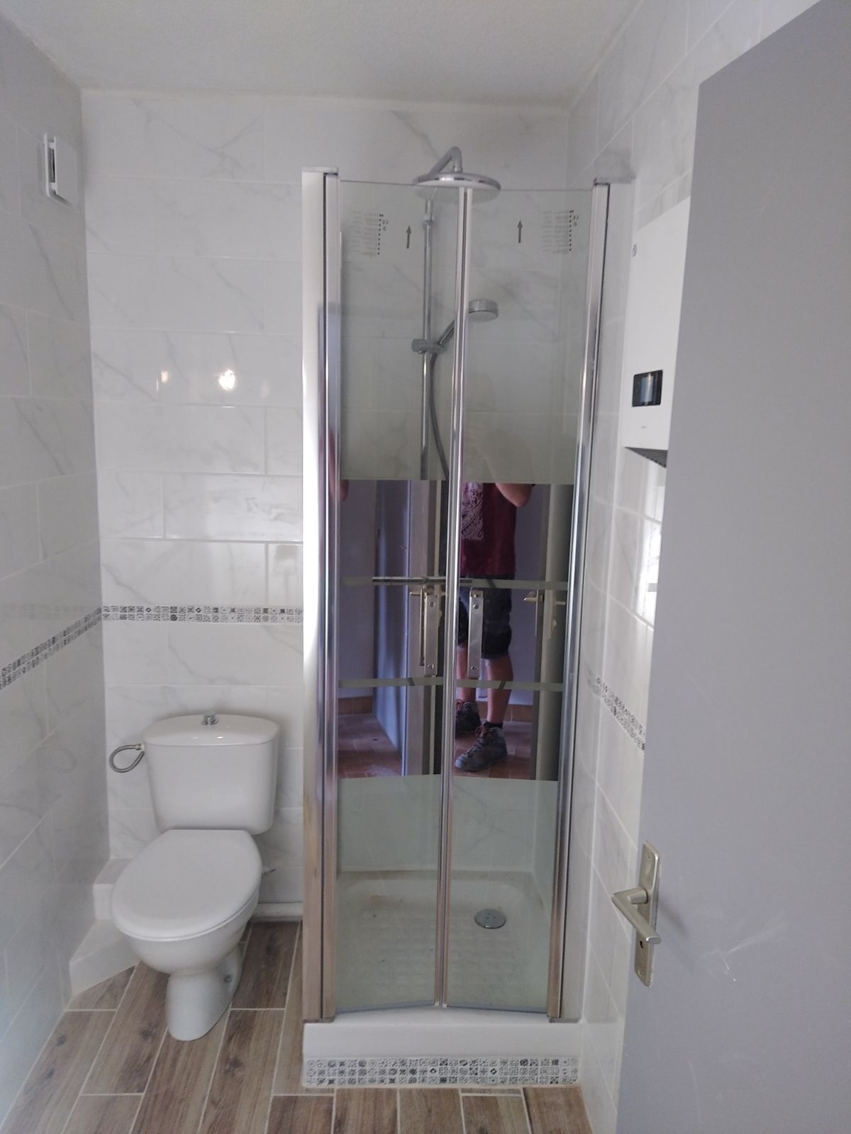 Ein Badezimmer mit einer gläsernen Duschkabine, einer Toilette und Fliesenboden.
