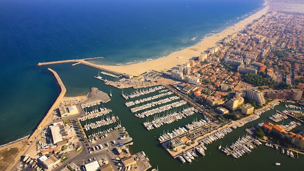 An aerial view of a coastal city with a marina, beach, and dense urban area.