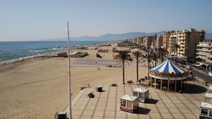 A beachside promenade with a carousel, palm trees, and a clear view of the sea.