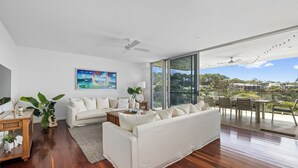 Ein geräumiges Wohnzimmer mit einem weißen Sofa, einem Couchtisch und einem großen Fenster mit Blick ins Freie.