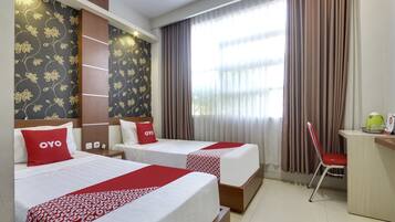 A hotel room with two beds, a desk, a chair, and a window with curtains.