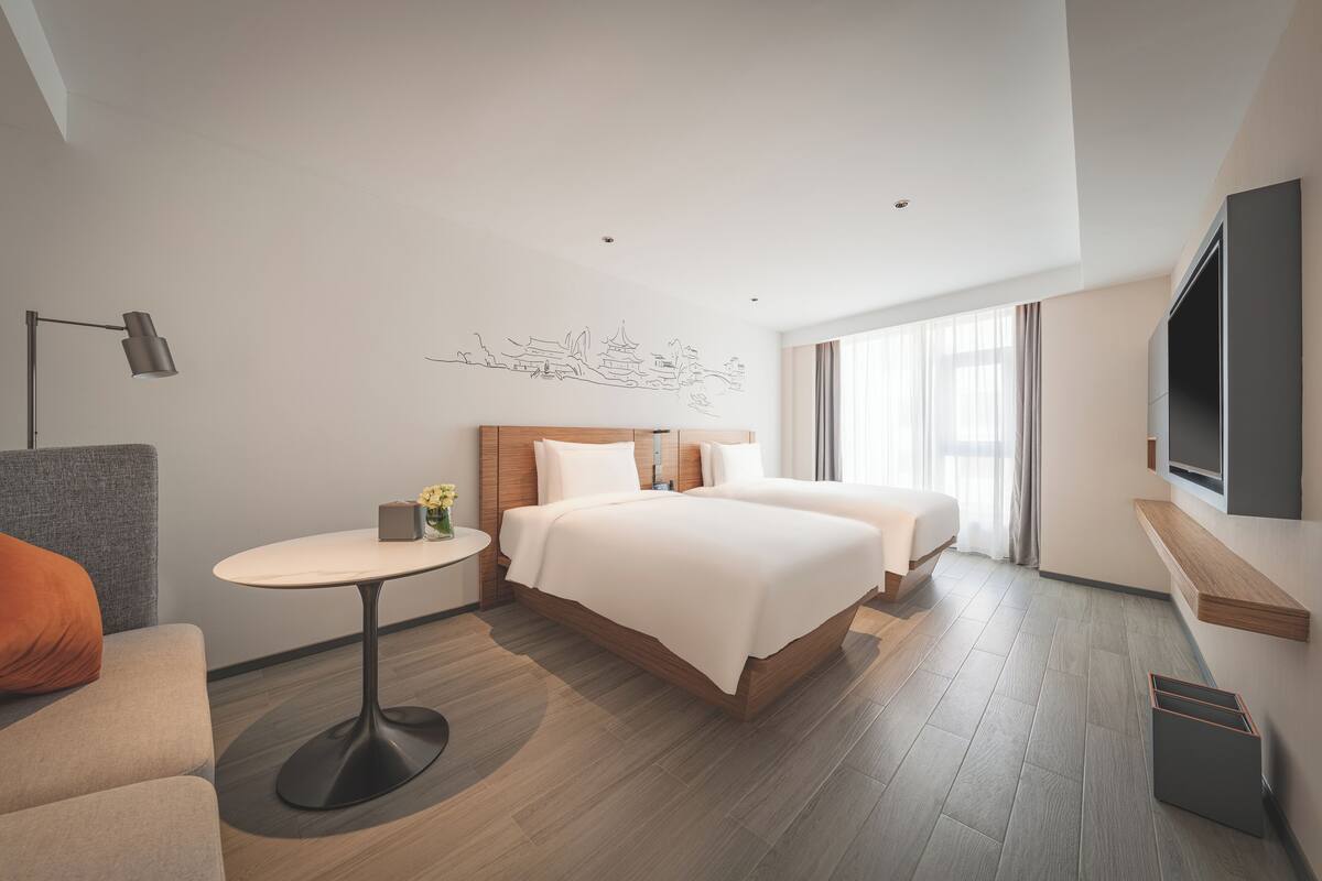 Une chambre d’hôtel moderne avec un grand lit, une petite table ronde, un canapé et un téléviseur fixé au mur.