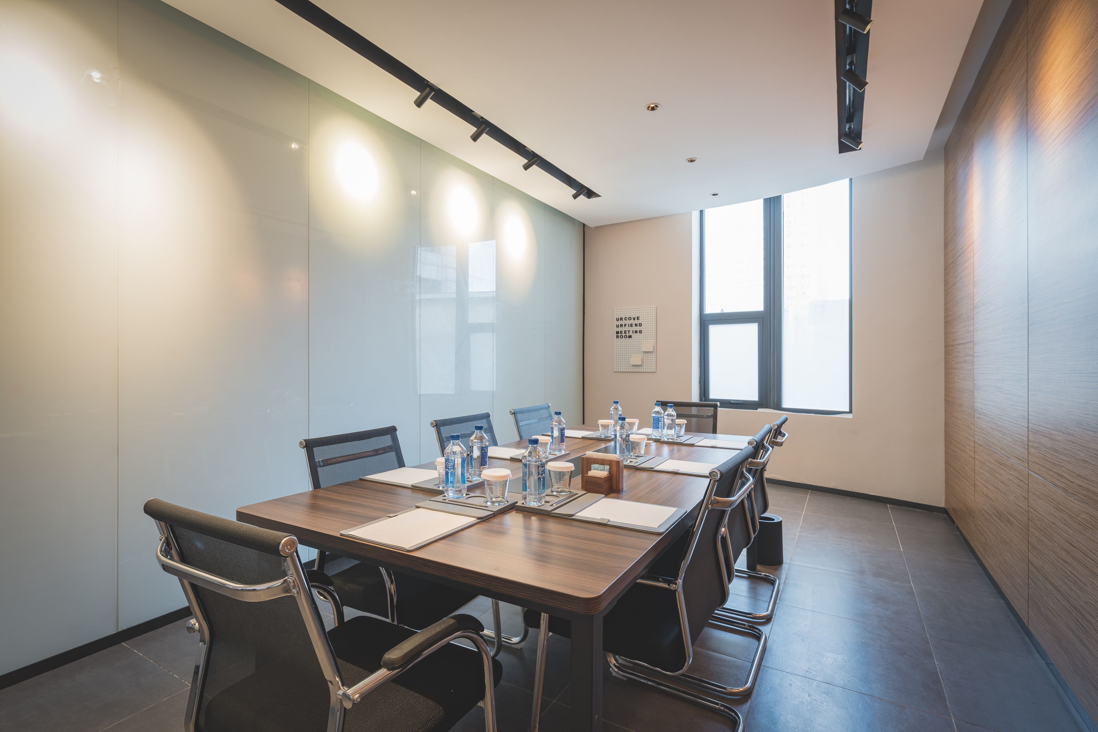 A conference room with a long table, chairs, water bottles, and a window.