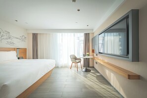 Habitación de hotel con una cama grande, un escritorio con silla, un televisor y una ventana con cortinas.