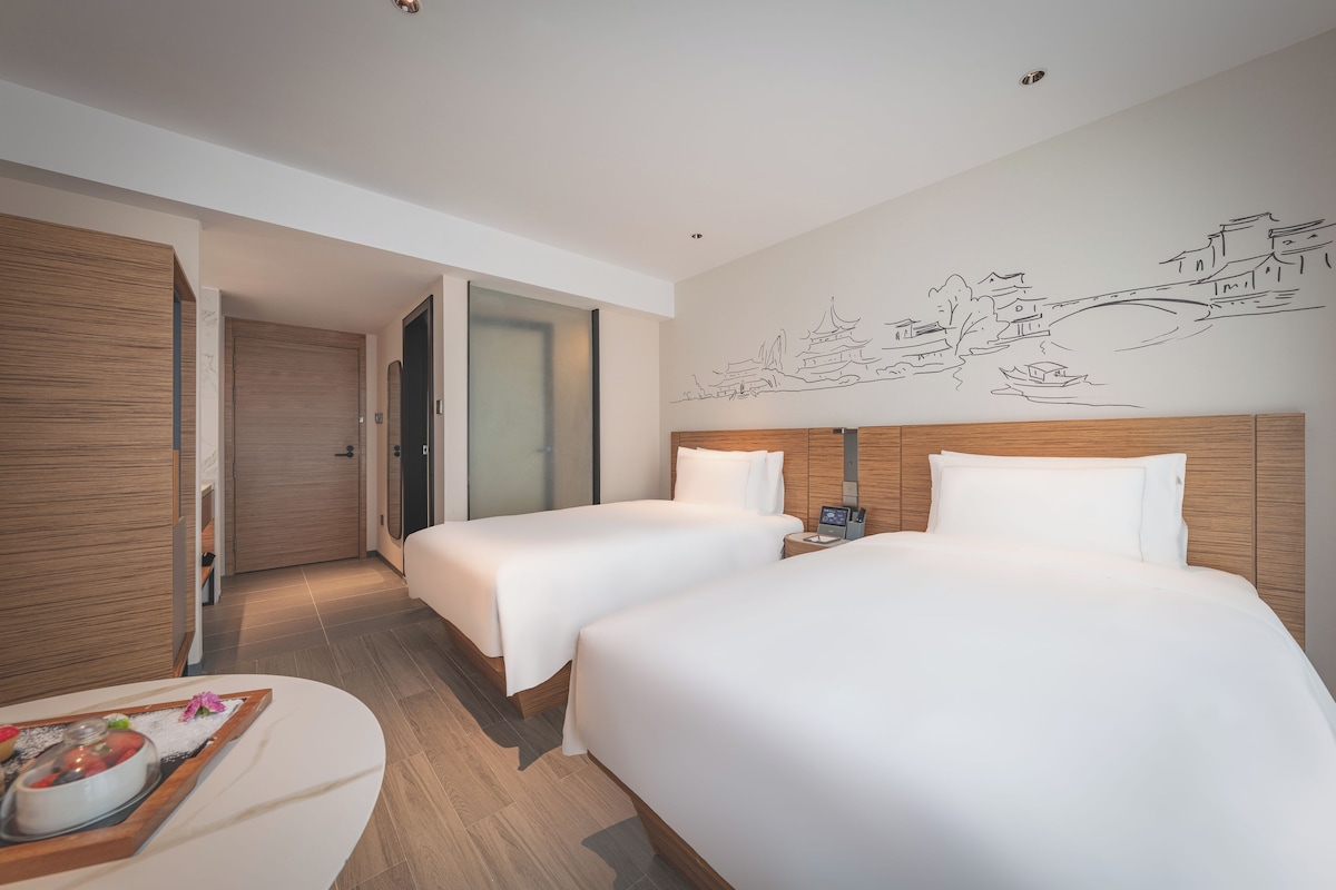 Une chambre d’hôtel avec deux lits, une tête de lit en bois, une fresque murale et une table de chevet avec un téléphone.