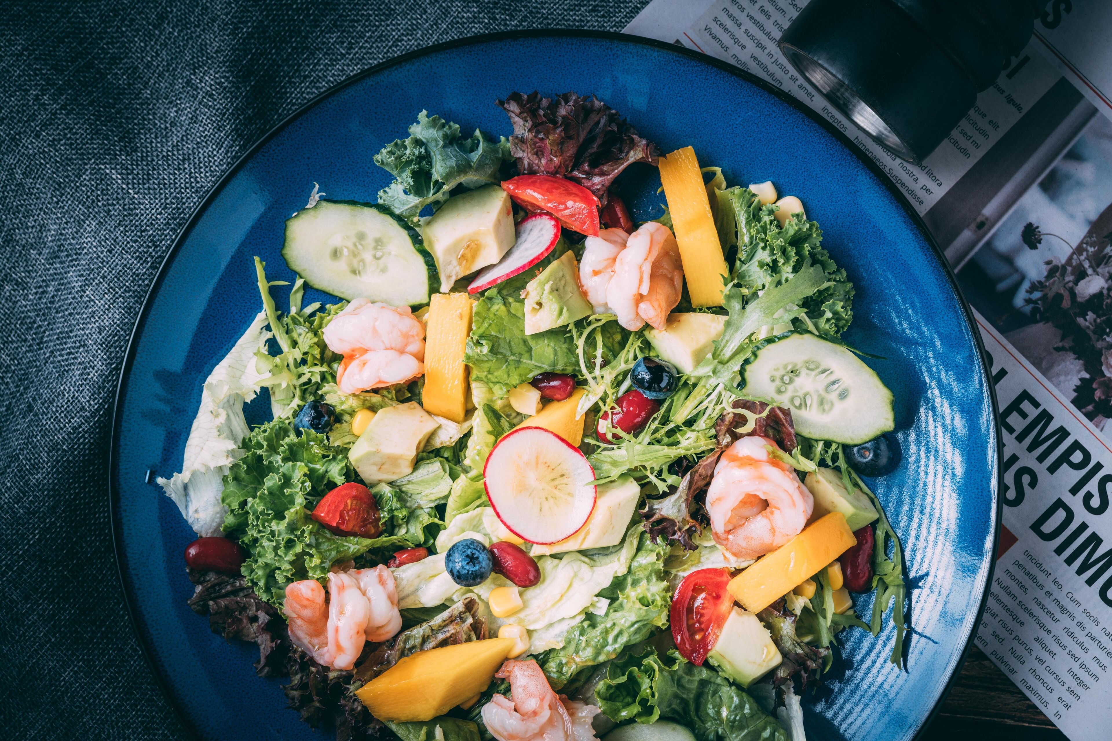 Une assiette bleue contenant une salade composée de crevettes, de fromage et de divers légumes.