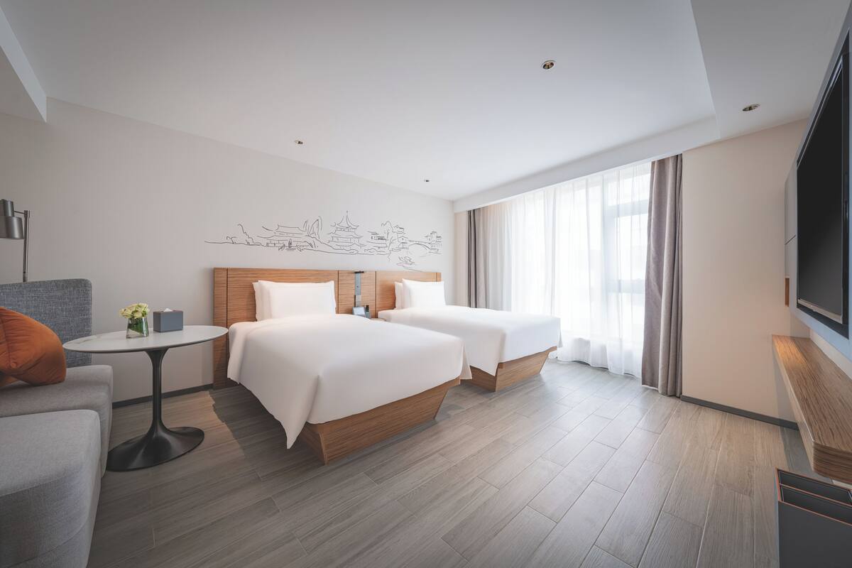 Une chambre d’hôtel avec deux lits, une petite table ronde, un canapé et un grand téléviseur.