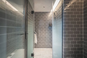 Un baño moderno con cabina de ducha de vidrio, paredes con azulejos y un perchero visible.