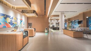 A modern hotel lobby with wooden reception desks, a colorful abstract mural, and a spacious layout with a central island and seating area. - UrCove by Hyatt Nanjing Downtown (Nanjing)