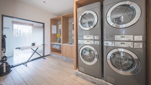 A modern laundry room with four stacked washing machines, a drying rack, and a small ironing station. - UrCove by Hyatt Nanjing Downtown (Nanjing)