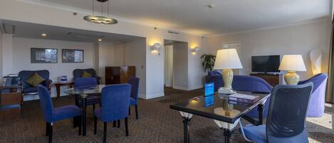 Quarto de hotel com área de refeições, televisão e mesa com computador.