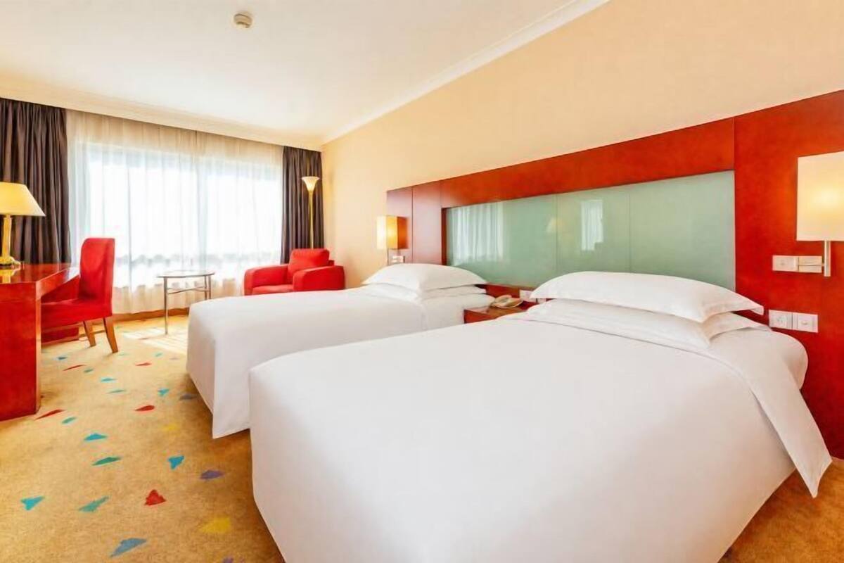 A hotel room with two beds, a desk, a chair, and a window with curtains.