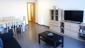 A living room with a sofa, a coffee table, a TV, and a dining area with chairs and a table. - Edificio Papa Luna (Peñiscola)