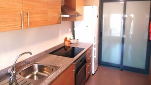 A kitchen with wooden cabinets, a stainless steel sink, a built-in oven, a refrigerator, and a sliding glass door. - Edificio Papa Luna (Peñiscola)