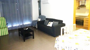 A compact living space with a sofa, a small table, a chair, and a kitchenette area. - Edificio Papa Luna (Peñiscola)