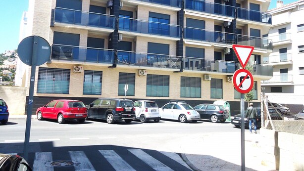 A multi-story building with balconies, parked cars, and a no parking sign. - Edificio Papa Luna (Peñiscola)