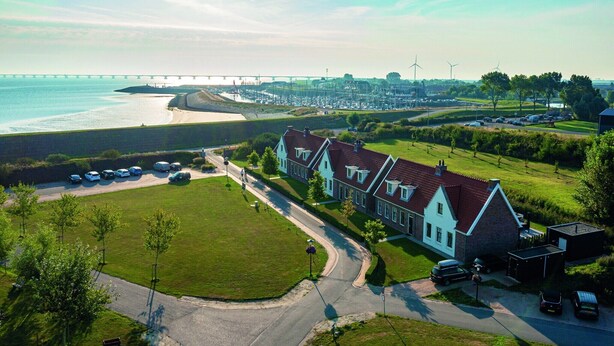 Ett bostadsområde med hus, en strand och en bro i bakgrunden.