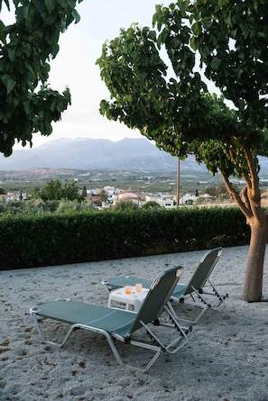 Eine Strandlounge mit zwei Stühlen aus Metall und einem Tisch mit Getränken, mit Blick auf eine reizvolle Landschaft aus Bergen und Gebäuden.