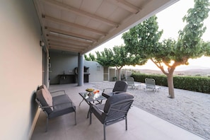 Eine Terrasse im Freien mit Esstisch und Stühlen, einem Grill und Blick auf Bäume und die Landschaft.