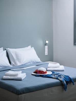 Ein ordentlich bezogenes Bett mit weißen Kissen, einer blauen Tagesdecke und gefalteten Handtüchern auf einer hellblauen Bettdecke.