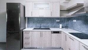 Une cuisine moderne dotée d’un réfrigérateur en acier inoxydable, de meubles de couleur bois clair, d’une plaque de cuisson noire et d’un pare-feu en marbre.