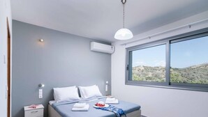 Une chambre moderne avec un grand lit, une table de chevet, une fenêtre donnant sur des collines et un appareil de climatisation.
