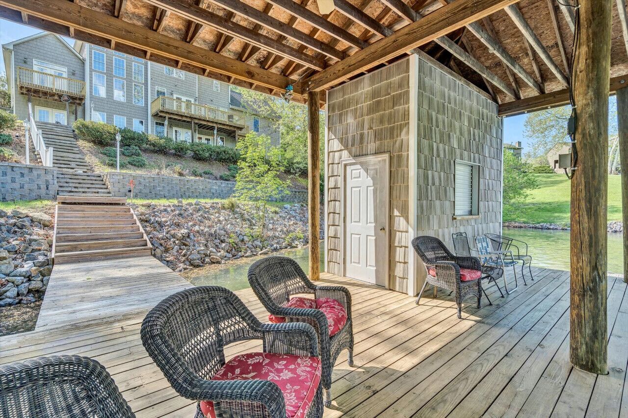 A covered outdoor deck with wicker chairs and a wooden staircase leading to a building.
