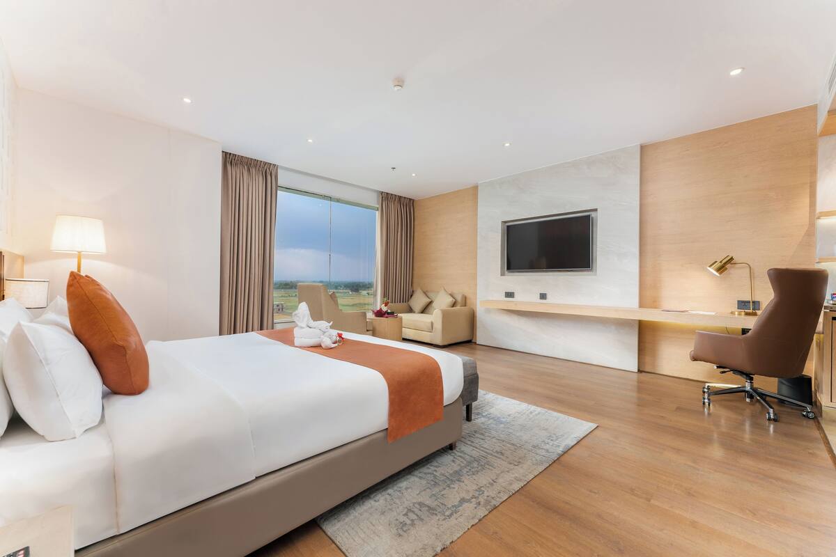 Een moderne hotelkamer met een groot bed, een bureau, een televisie en uitzicht op de omgeving.