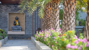A statue of a seated figure in a niche, surrounded by a garden with flowering plants and a palm tree. - Siddhartha Vilasa (Siddharthanagar)