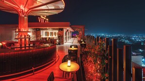 A rooftop bar with a view of the city at night, featuring a bar counter, seating area, and a large umbrella structure. - Siddhartha Vilasa (Siddharthanagar)