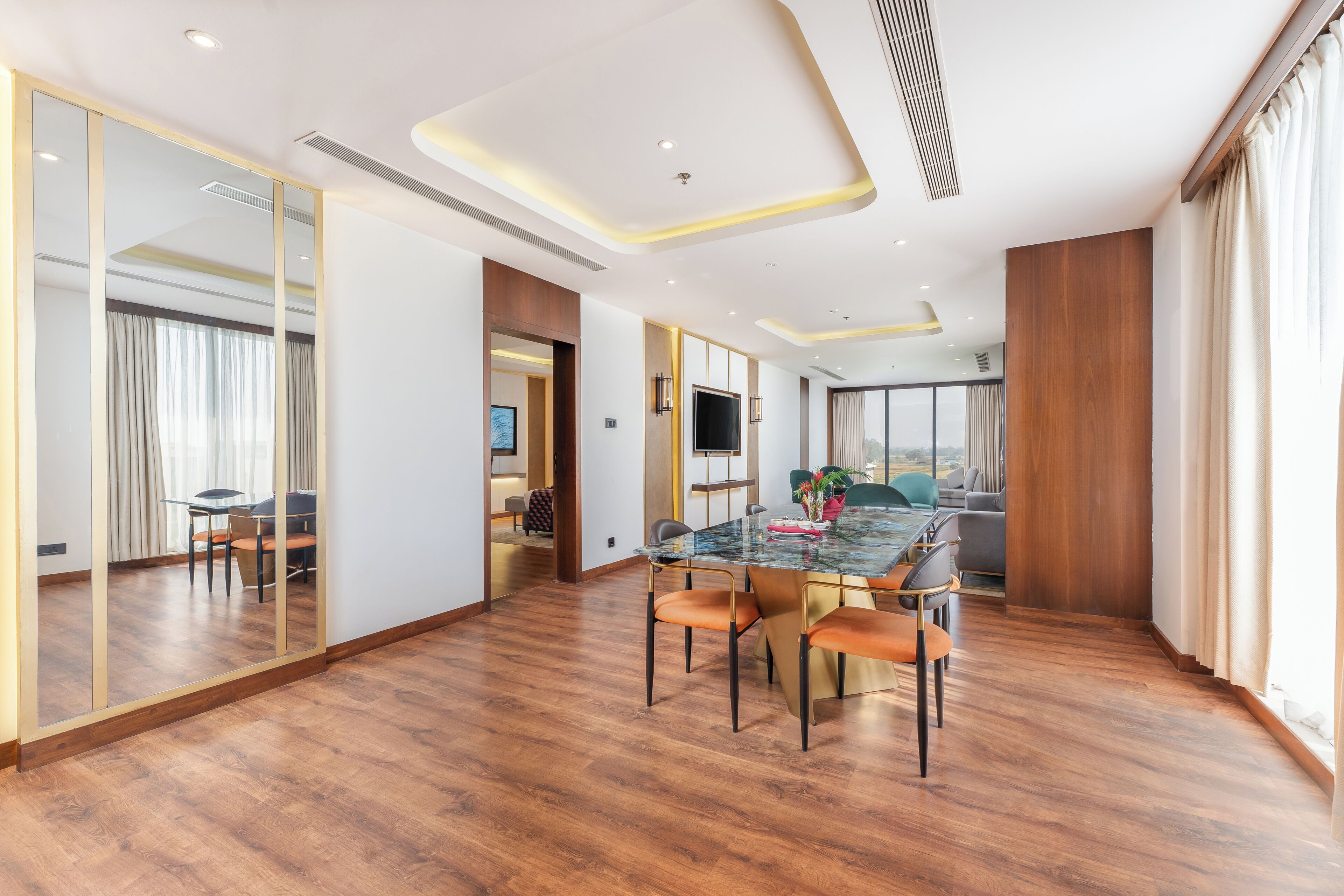 A modern dining area with a glass table, wooden flooring, and a large mirror.