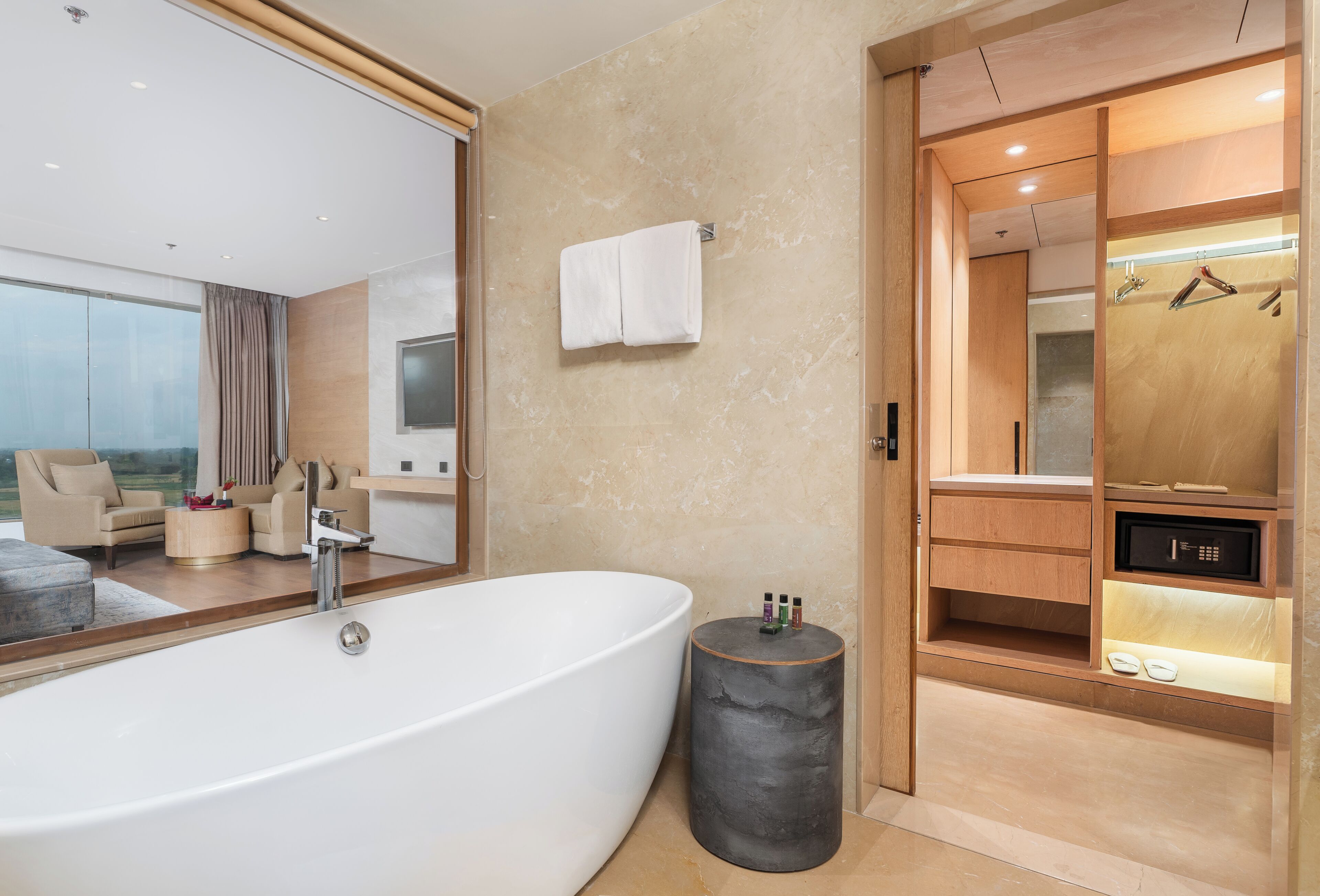 A modern bathroom with a large bathtub, a round stool, a towel rack, and a wooden vanity with a mirror.