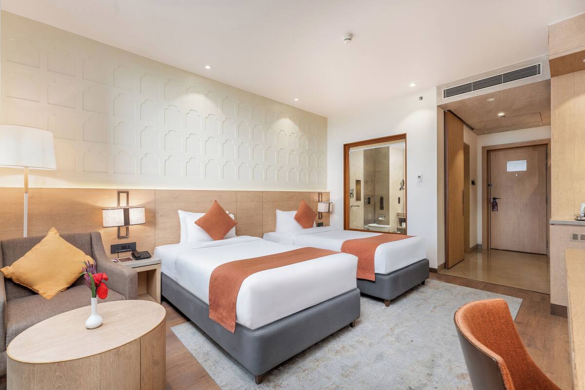 Een hotelkamer met twee bedden, een bank, een tafeltje, een spiegel en een deur naar de badkamer.