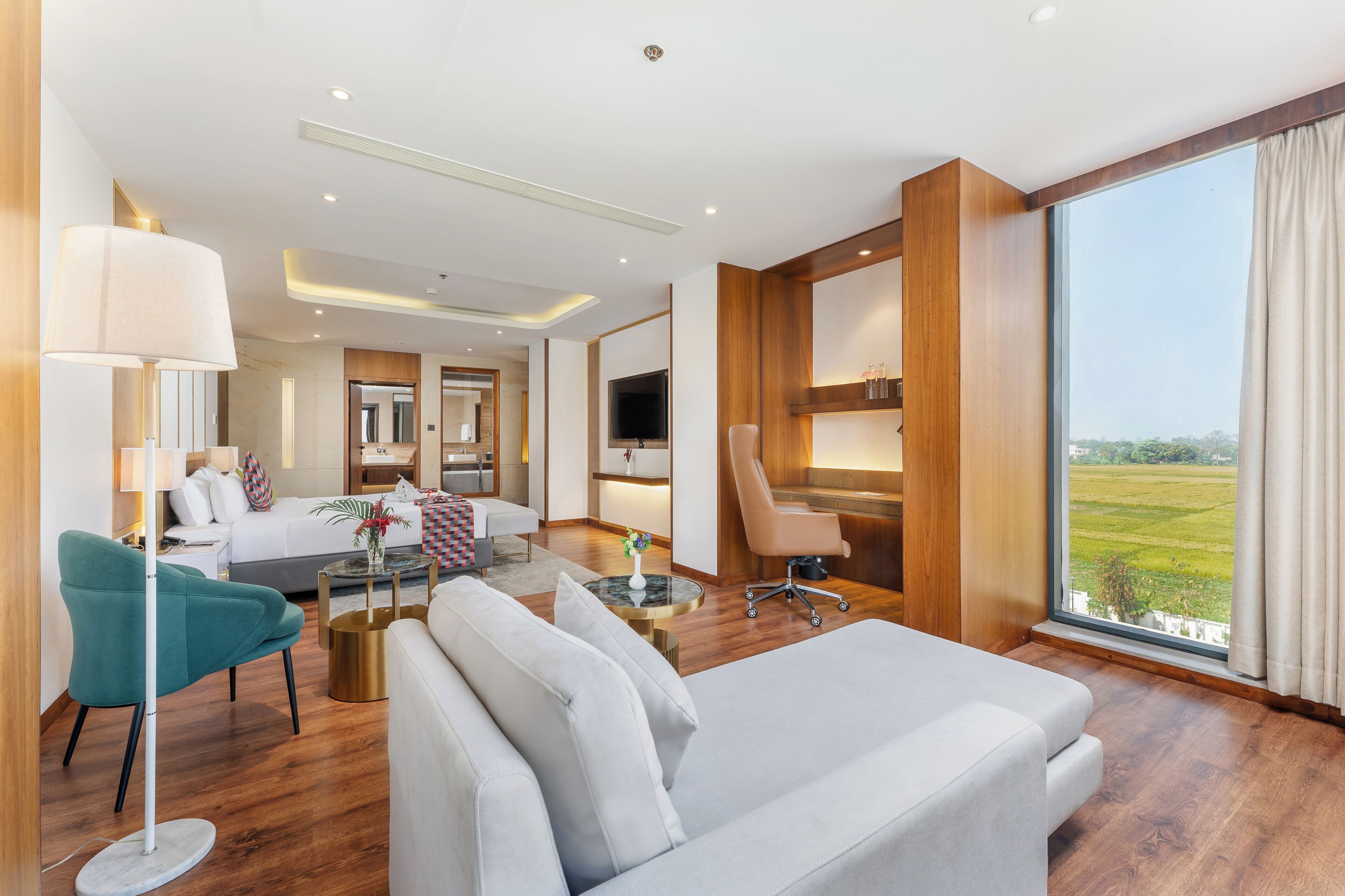 A modern hotel room with a large bed, a sofa, a desk, a chair, and a TV.