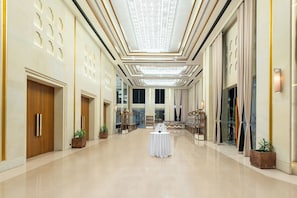 A spacious hotel corridor with a central round table, large windows, and a high ceiling with a decorative light fixture. - Siddhartha Vilasa (Siddharthanagar)