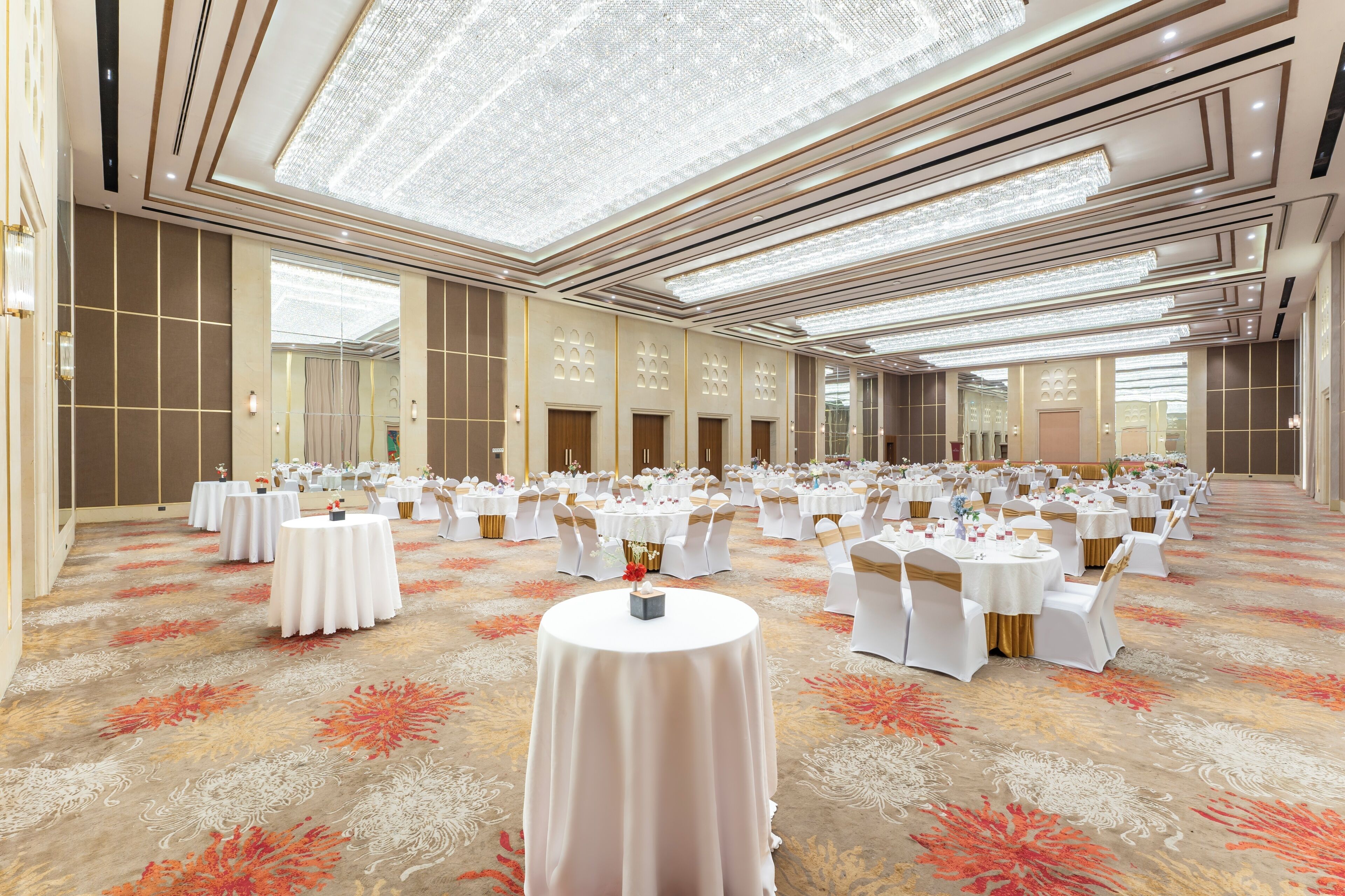 Un salón de banquetes con mesas redondas, manteles blancos y sillas doradas.