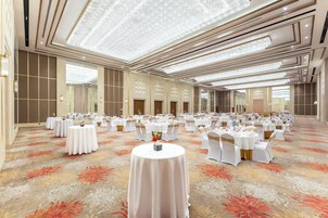 Un salón de banquetes con mesas redondas, manteles blancos y sillas doradas.