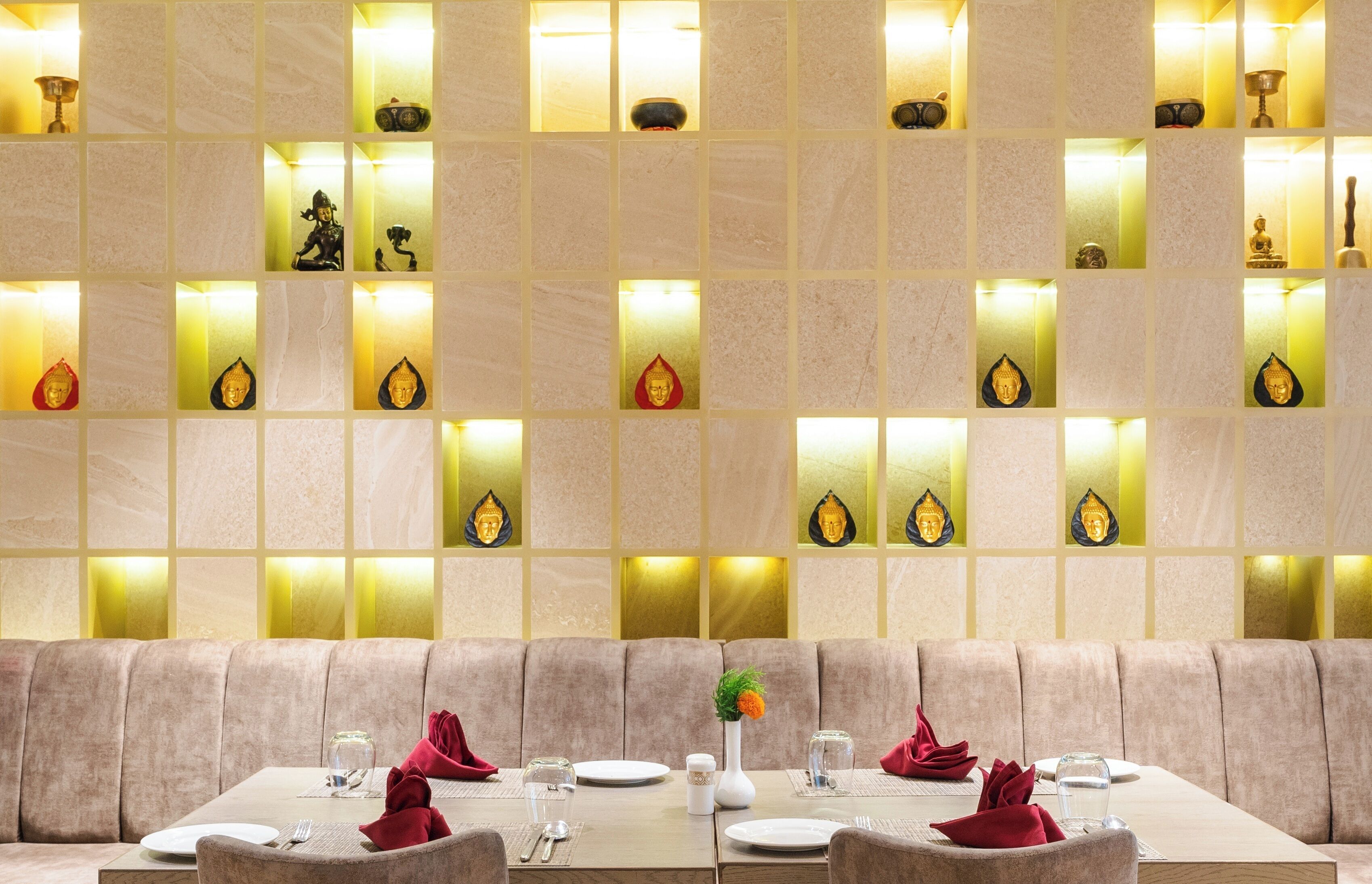 A dining area with a long table, cushioned seating, and a wall with illuminated panels displaying various objects.