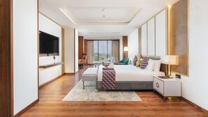 A modern hotel room with a large bed, a TV, a desk, and a view of the city. - Siddhartha Vilasa (Siddharthanagar)