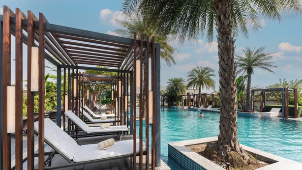 A pool area with lounge chairs, a pergola, and palm trees. - Siddhartha Vilasa (Siddharthanagar)